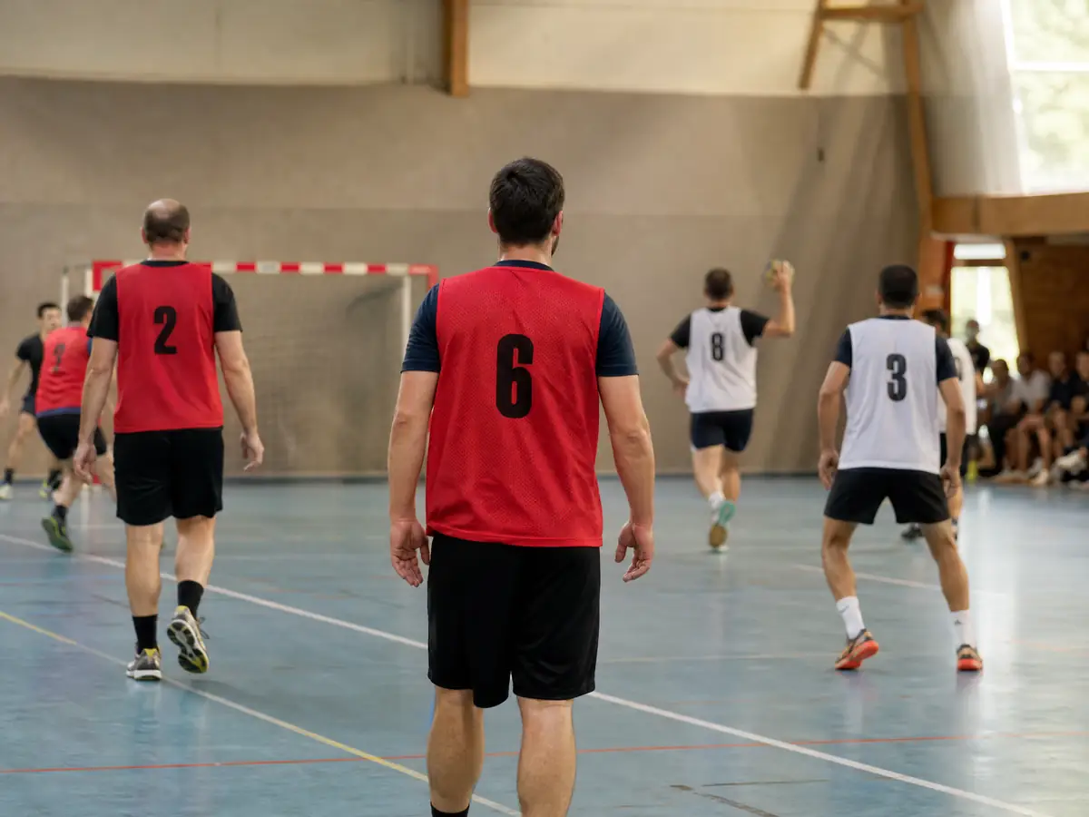 Joueurs adultes vus de dos dans un gymnase, en chasubles rouges et blanches numérotées